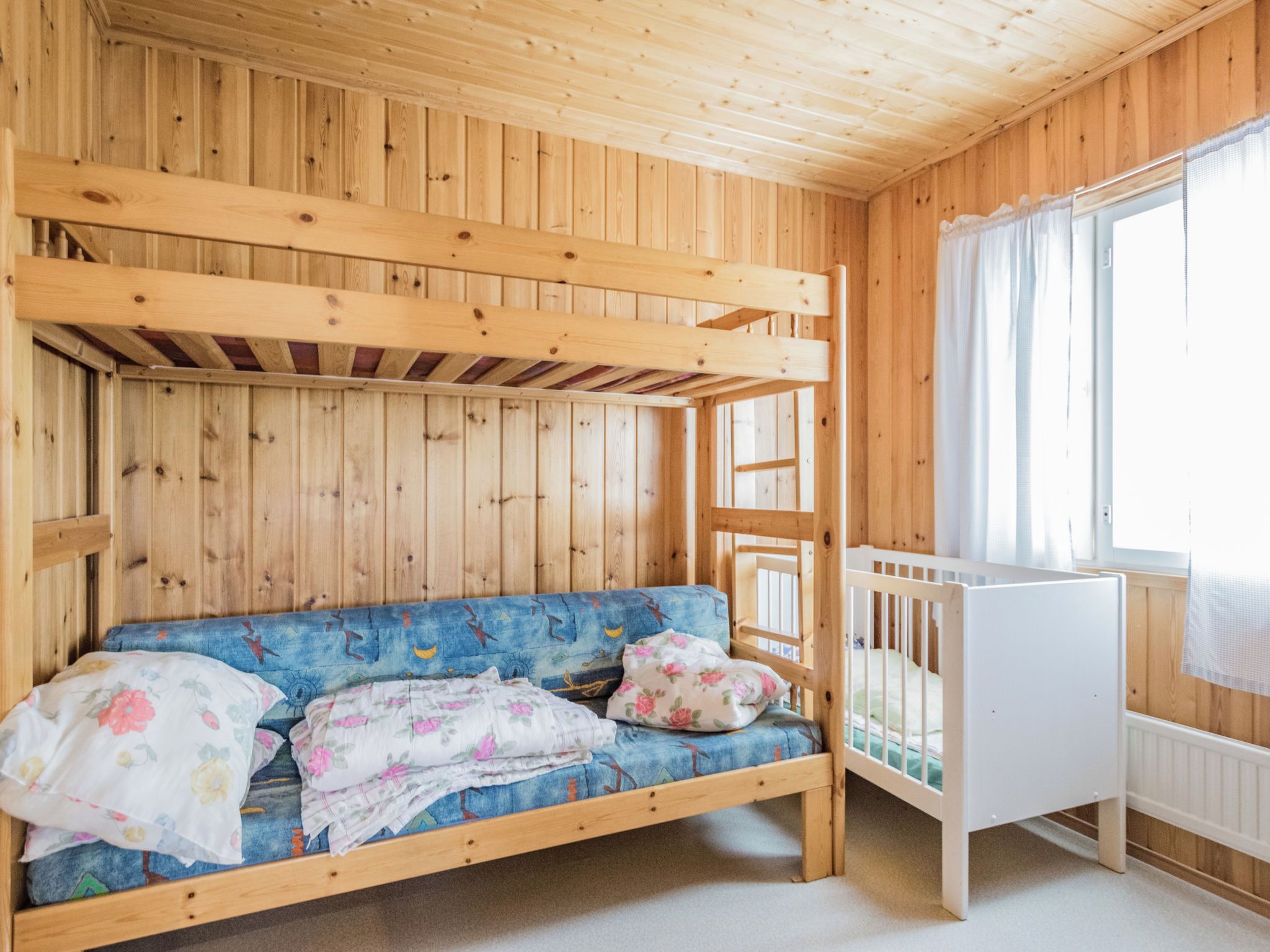 A wooden room with a bunk bed, a sofa, and a crib.