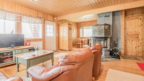 L’intérieur chaleureux d’un chalet avec un plafond en bois, une télévision, un canapé, une cheminée et un coin repas.