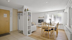 A modern, well-lit room with a dining area, a built-in bookshelf, and a television. - Apartment Ruggli by Interhome (Churwalden)