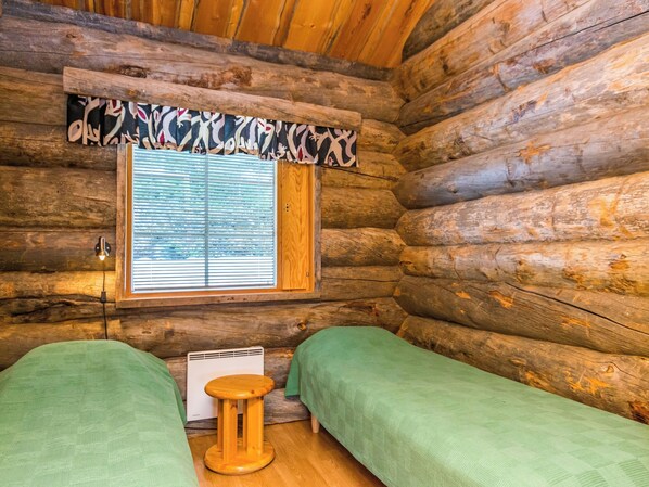 A log cabin room with two beds, a small wooden stool, and a window with blinds.