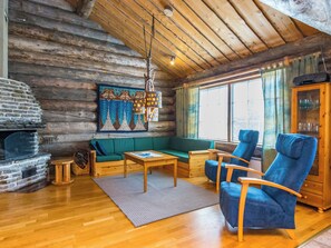A cozy log cabin interior with a stone fireplace, a green sofa, blue armchairs, and a wooden cabinet. - Kelokieppi by Interhome (Kuusamo)