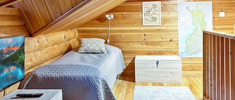A cozy attic bedroom with a bed, a nightstand, a dresser, a map, and a television.