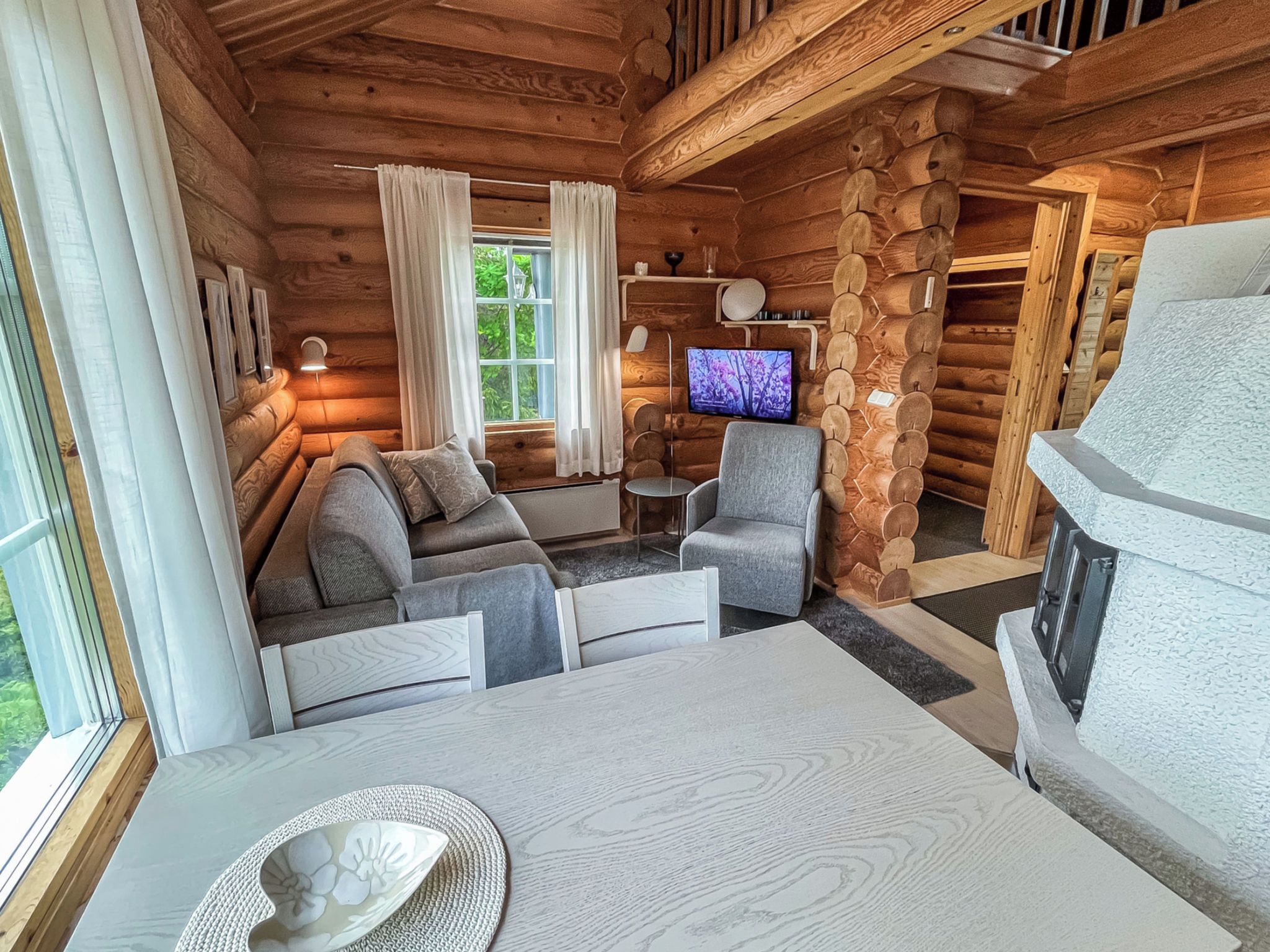 L’intérieur d’un chalet confortable en bois, avec un canapé, des fauteuils, une table à manger, un téléviseur et une cheminée.