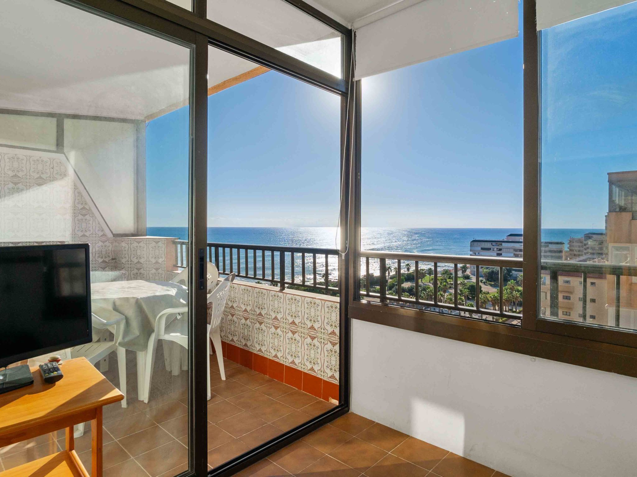 Un balcón con vista al mar, un televisor sobre una mesa y una silla.