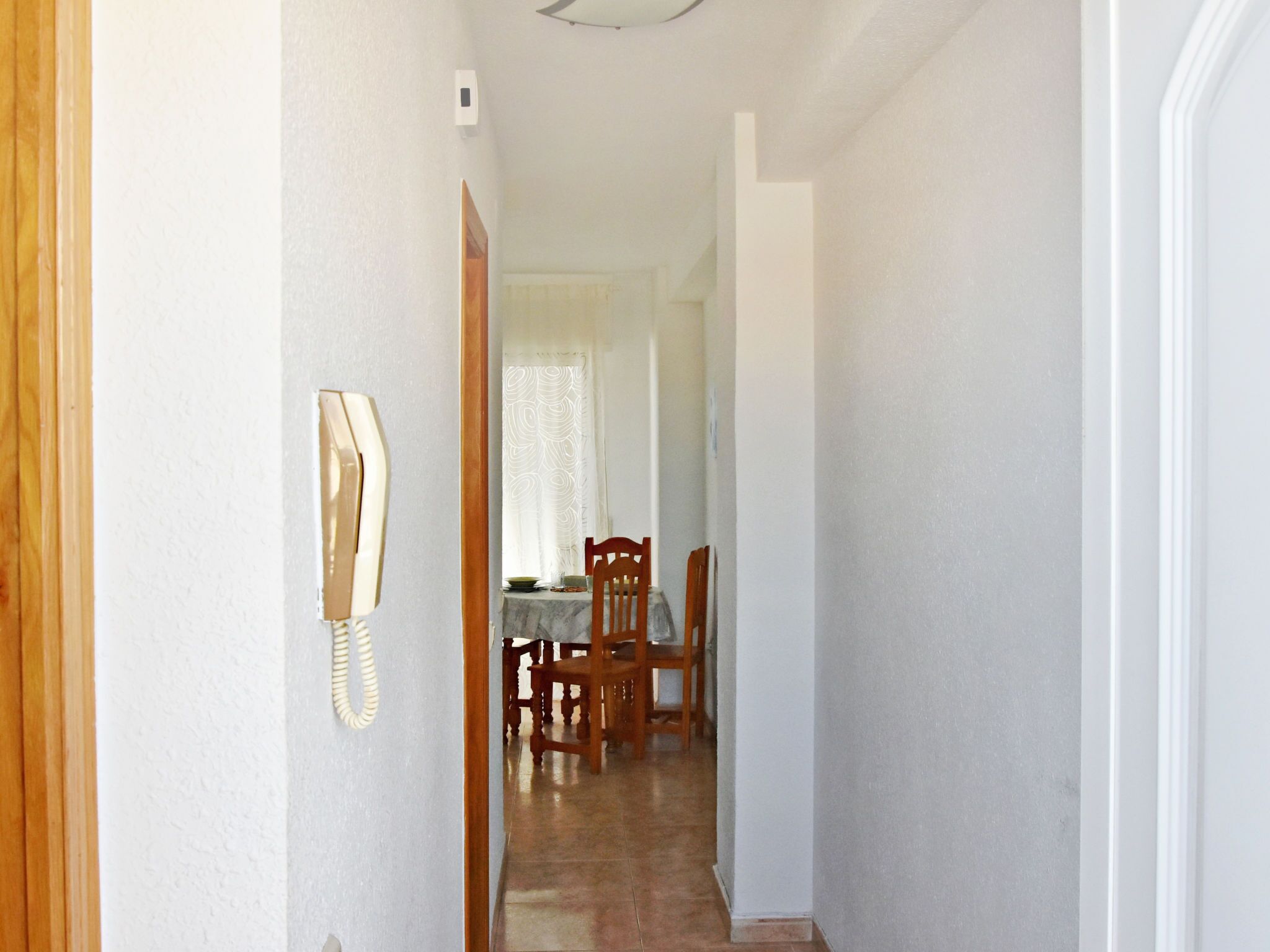 A hallway with a wooden door, a telephone, and a dining area with chairs and a table.