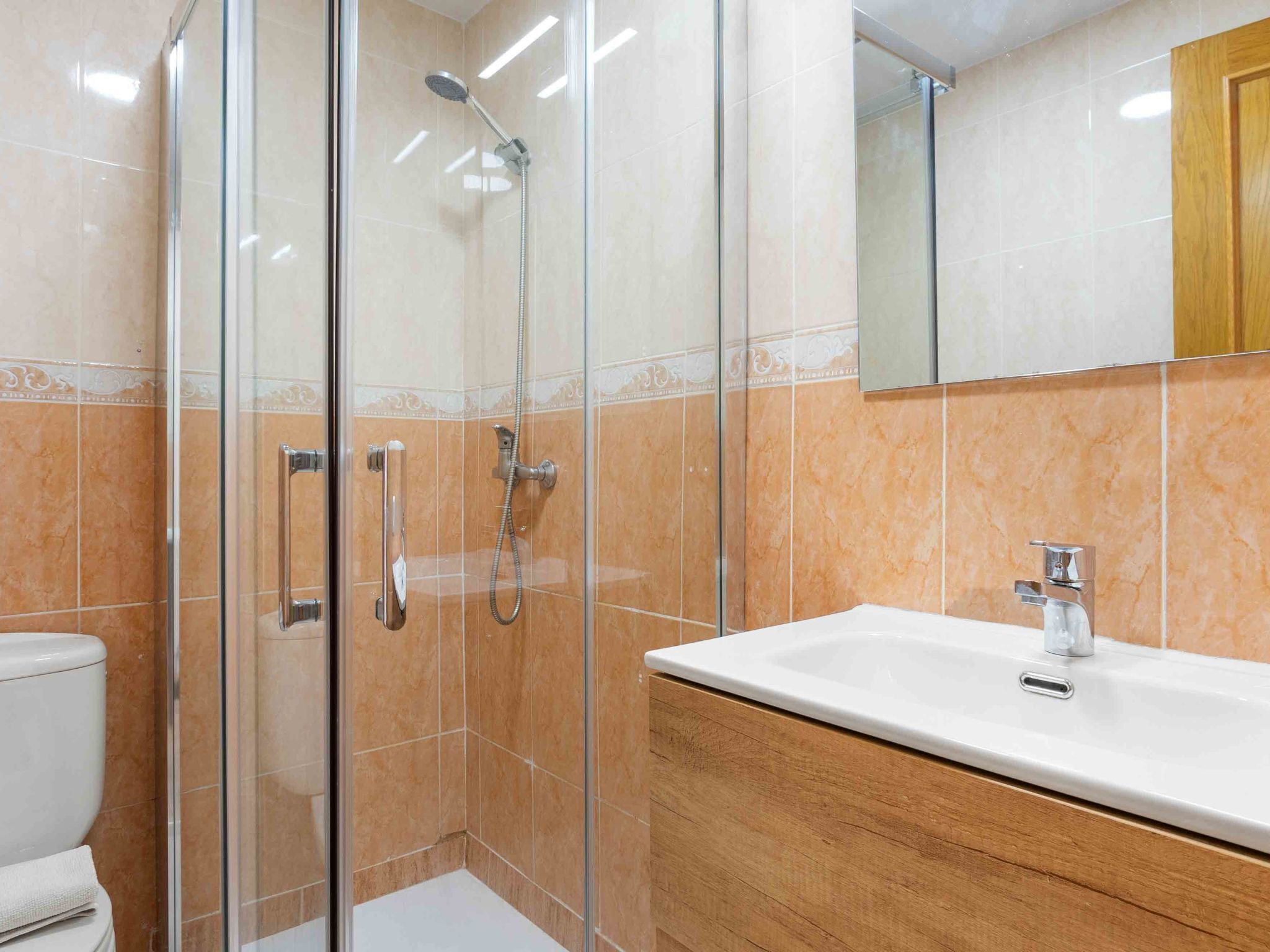 A bathroom with a glass-enclosed shower, a white sink, and a wooden vanity.