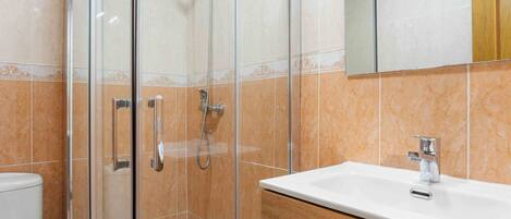 A bathroom with a glass-enclosed shower, a white sink, and a wooden vanity.