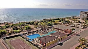Ein Hotel an der Küste mit Tennisplatz, Schwimmbad und Meerblick.