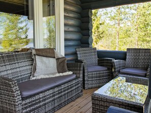 Une cabane en rondins avec des meubles en osier, notamment un canapé et des fauteuils, sur une terrasse en bois.