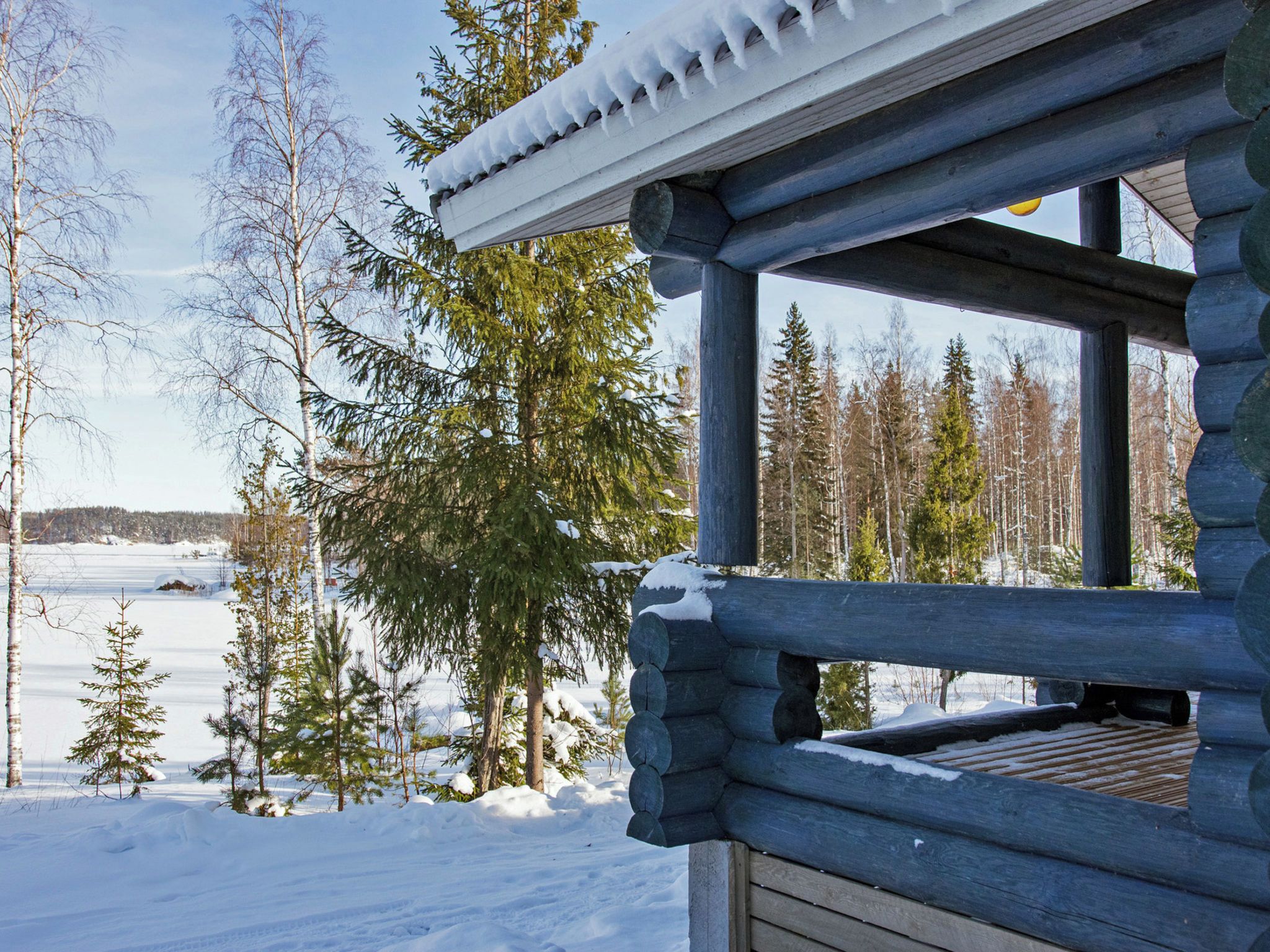 A log cabin with a snow-covered roof, surrounded by trees and a snowy landscape.