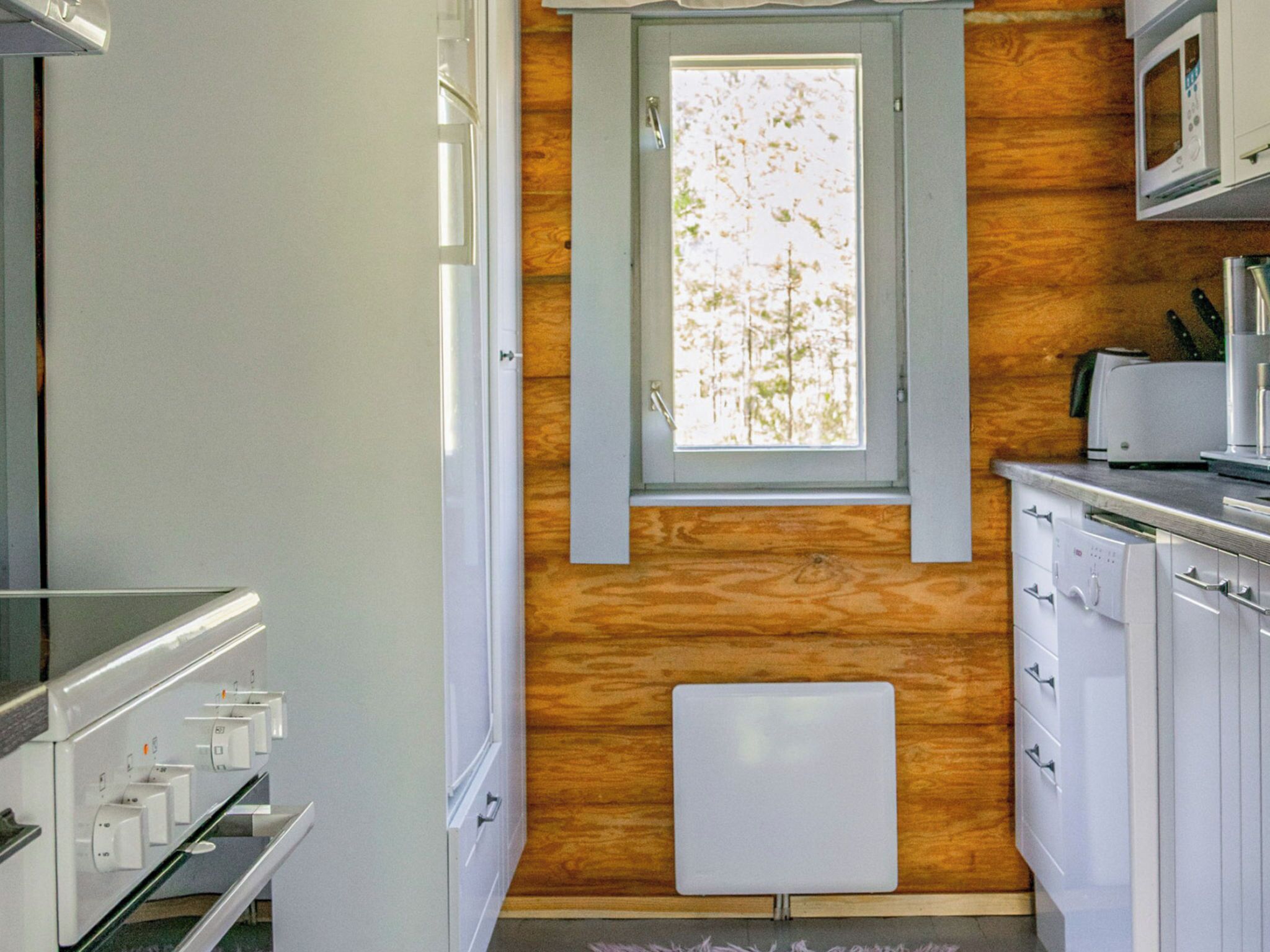 A compact kitchen with a window, wooden wall paneling, a microwave, and a dishwasher.