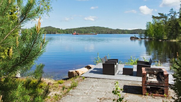 A lakeside deck with outdoor furniture and a view of a lake and distant ship. - Vacation home Norppa by Interhome (Puumala)