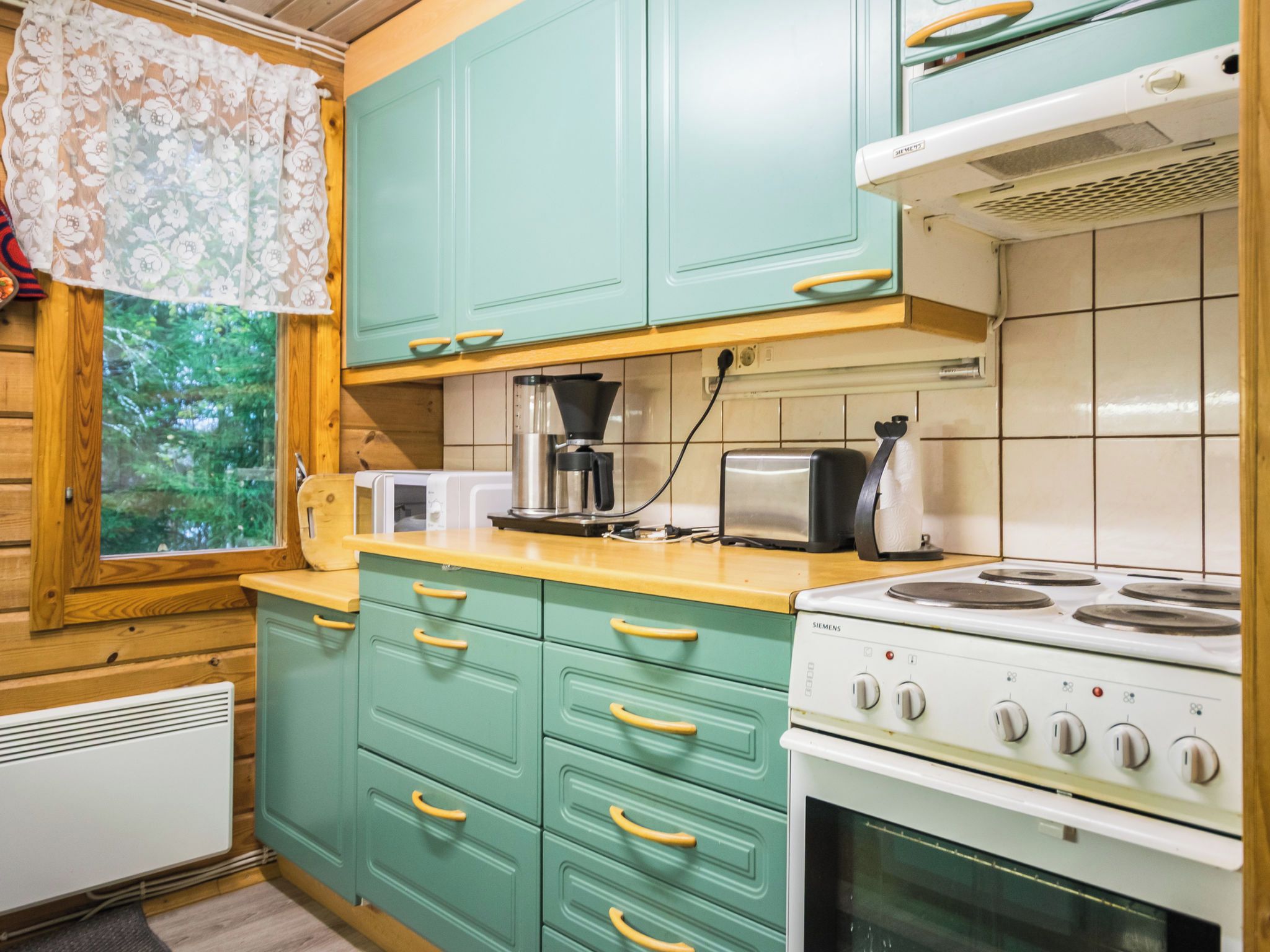 A kitchen with teal cabinets, a white stove, and a window with a view of greenery.