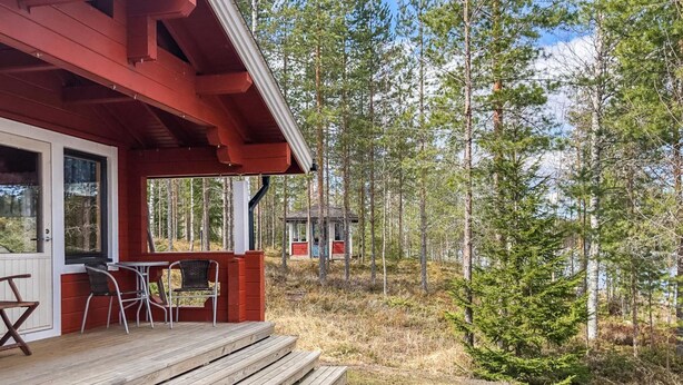 Una terraza de madera con mobiliario exterior, una zona cubierta con mesa y sillas, y un bosque de fondo.