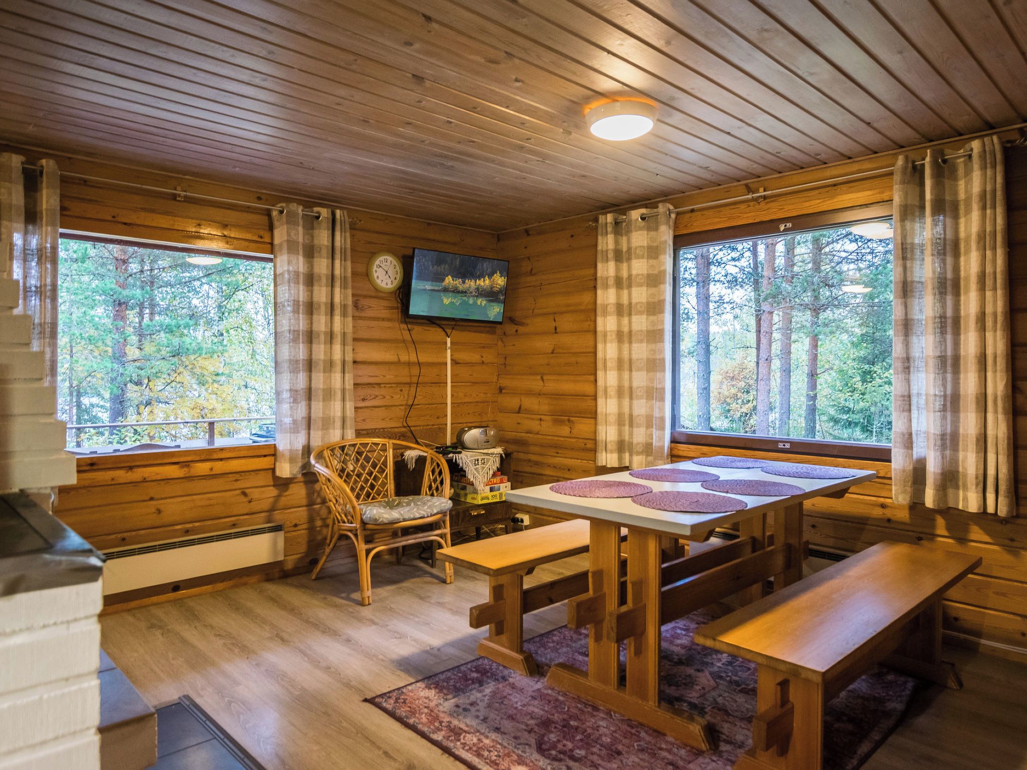 A cabin interior with wooden walls, a television mounted on the wall, a dining table with benches, and a chair.
