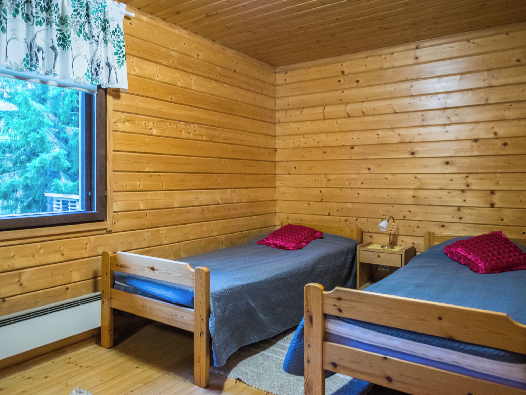 Una cabaña con dos literas de madera, una ventana con vista a árboles y una mesita de noche con una lámpara.