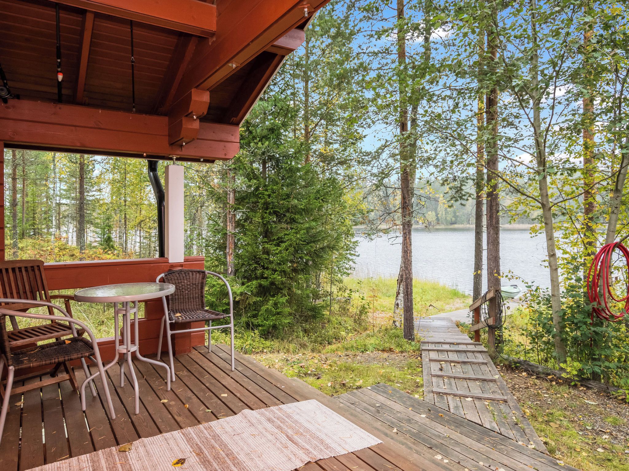 A wooden deck with a table and chairs, overlooking a lake surrounded by trees.