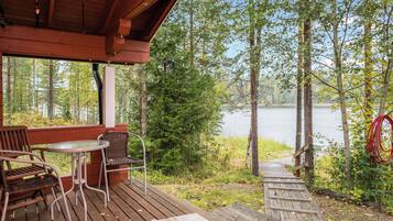 A wooden deck with a table and chairs, overlooking a lake surrounded by trees.