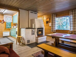 A cozy cabin interior with a fireplace, wooden walls, a dining area, and a kitchen with a window. - Iltaniemi by Interhome (Enonkoski)