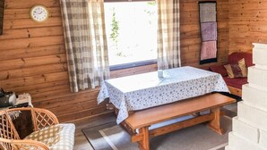 Interior acogedor de una cabaña con detalles de madera, una mesa con mantel estampado, un banco, una silla de mimbre y una ventana con cortinas.