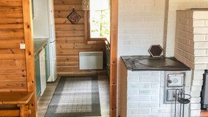 Un pasillo estrecho con paredes de madera, una ventana pequeña con cortina floral, un radiador y una zona de cocina con estufa y fregadero.