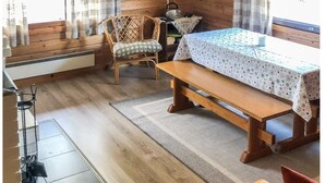 Una habitación acogedora tipo cabaña con paredes de madera, una cama con colcha estampada, una silla, una mesa, un televisor y un reloj en la pared.