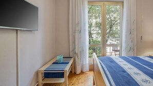 Ett sovrum med en säng, ett litet bord, en bänk och ett fönster med gardiner.