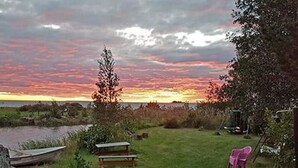 A grassy outdoor area with a bench and two chairs, overlooking a body of water and a sunset. - Soukonranta by Interhome (Pori)