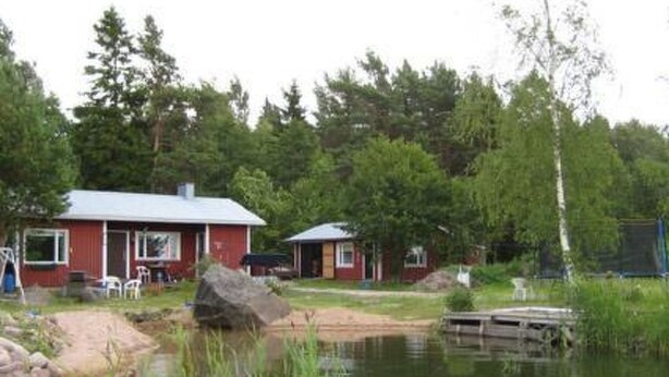 A cabin with a red exterior, a dock extending into a pond, surrounded by dense trees. - Soukonranta by Interhome (Pori)