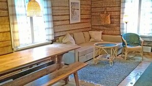 Ein gemütliches Blockhaus-Interieur mit einer hölzernen Bank, einem Sofa, einem kleinen runden Tisch und einem Korbstuhl.