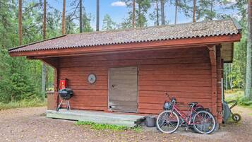 A wooden cabin with a porch, a bicycle, and a grill.