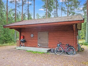Une cabane en bois avec une véranda, un vélo et un barbecue.