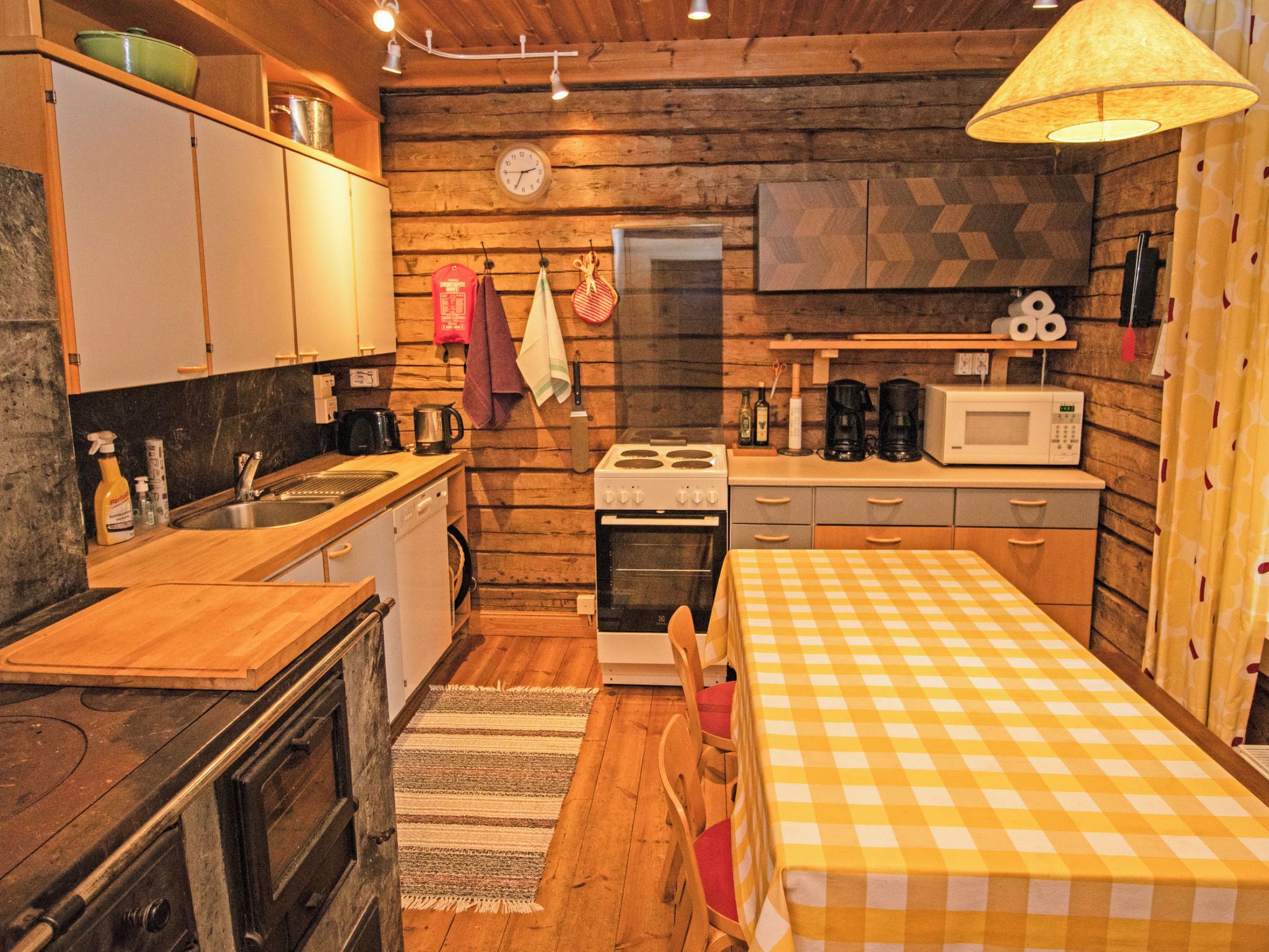 A compact kitchen with wooden walls, a stove, a microwave, and a sink.