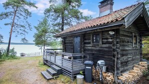Un chalet rustique doté d’une terrasse en bois, d’une cheminée et offrant une vue sur le lac.