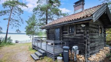A rustic cabin with a wooden deck, a chimney, and a view of the lake.