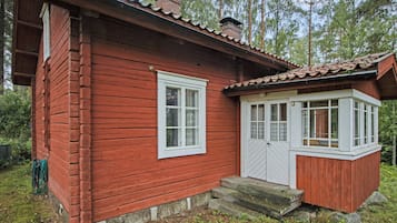 A red wooden cabin with a white door and windows, a small porch, and a chimney.