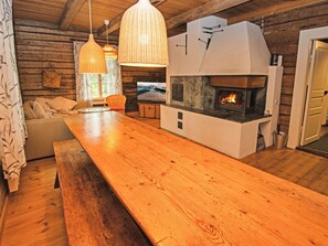 A cozy cabin interior with a wooden dining table, wicker pendant lights, a stone fireplace, and a television. - Villa pettu by Interhome (Salo)