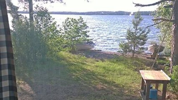 Blick auf einen See mit einem kleinen Holztisch und einem blauen Behälter am Ufer.