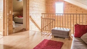 Interior de una cabaña de madera con un dormitorio en altillo, una escalera y una zona de estar acogedora.