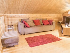 Una habitación acogedora con un sofá, un taburete pequeño, un televisor y una alfombra roja.