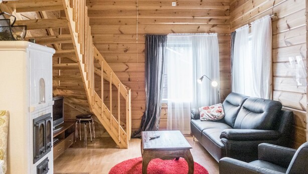 Interior acogedor de una cabaña con una escalera de madera, un sofá, una mesa de centro y una chimenea.