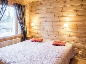 A room with a wooden paneled wall, a bed with a white quilt, two red pillows, and two wall-mounted lamps.