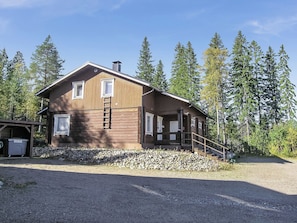 A two-story wooden cabin with a gravel driveway and a wooden deck.