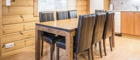 Une pièce aux murs lambrés, comprenant une table à manger et des chaises, une horloge, ainsi qu’un coin cuisine équipé d’appareils électroménagers.
