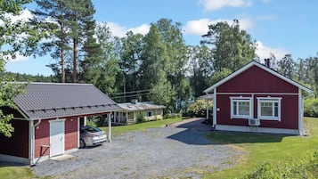 A red building with a car parked in front, surrounded by trees and a gravel driveway.