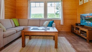 A cozy cabin interior with a wooden ceiling, a sofa, a coffee table, a TV on a wooden stand, and a window with curtains. - Talvikki by Interhome (Kuopio)