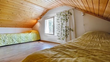 A small, cozy attic bedroom with wooden slats on the ceiling, a window with curtains, and two beds.