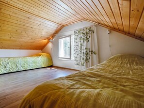 Een knus zolderkamertje met houten latten op het plafond, een raam met gordijnen en twee bedden.
