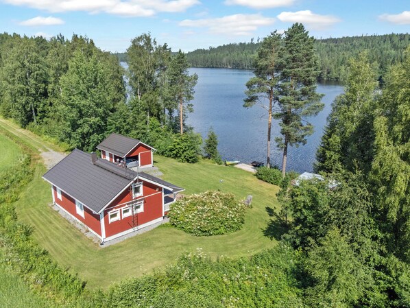 A red house with a garage, surrounded by a well-maintained lawn and a lake.