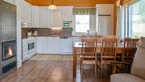 A modern kitchen with white cabinets, a central island, a fireplace, and a dining area with wooden chairs. - Talvikki by Interhome (Kuopio)